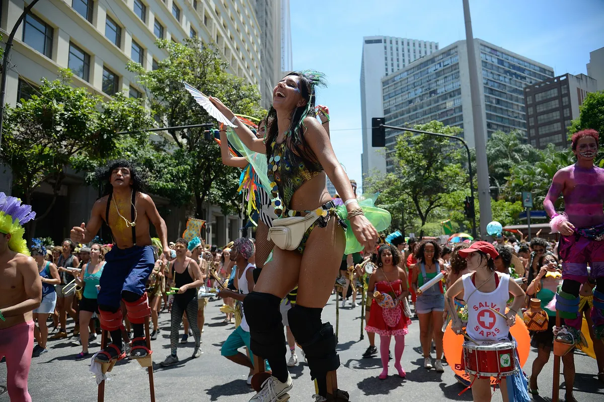 A dense, joyful crowd dances behind musicians through a Rio street during a daytime bloco