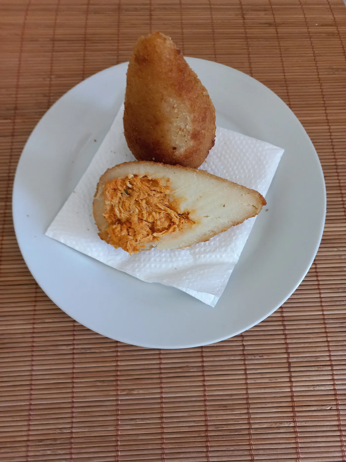Two teardrop-shaped coxinhas with a crisp golden crust, one bitten to show the chicken filling