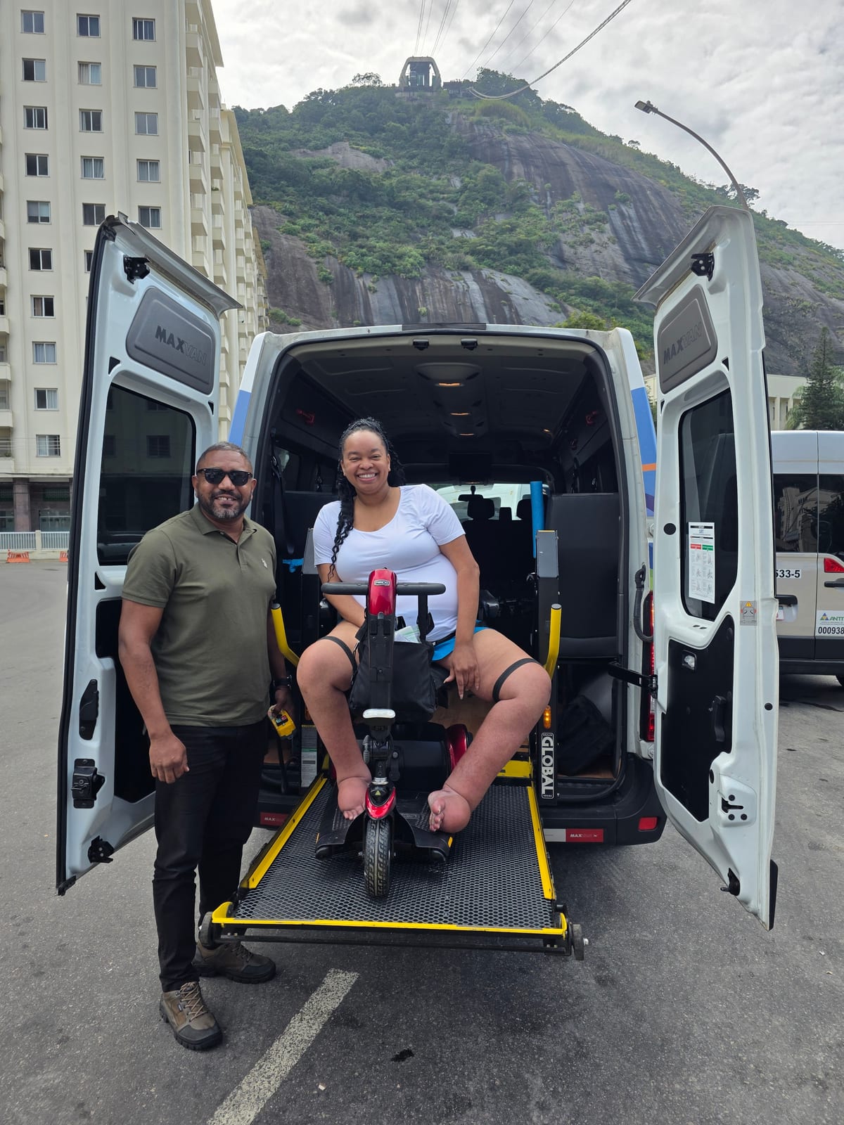 A guest using a mobility scooter boards an accessible tour van with a Trip in Brazil guide, below Sugarloaf Mountain